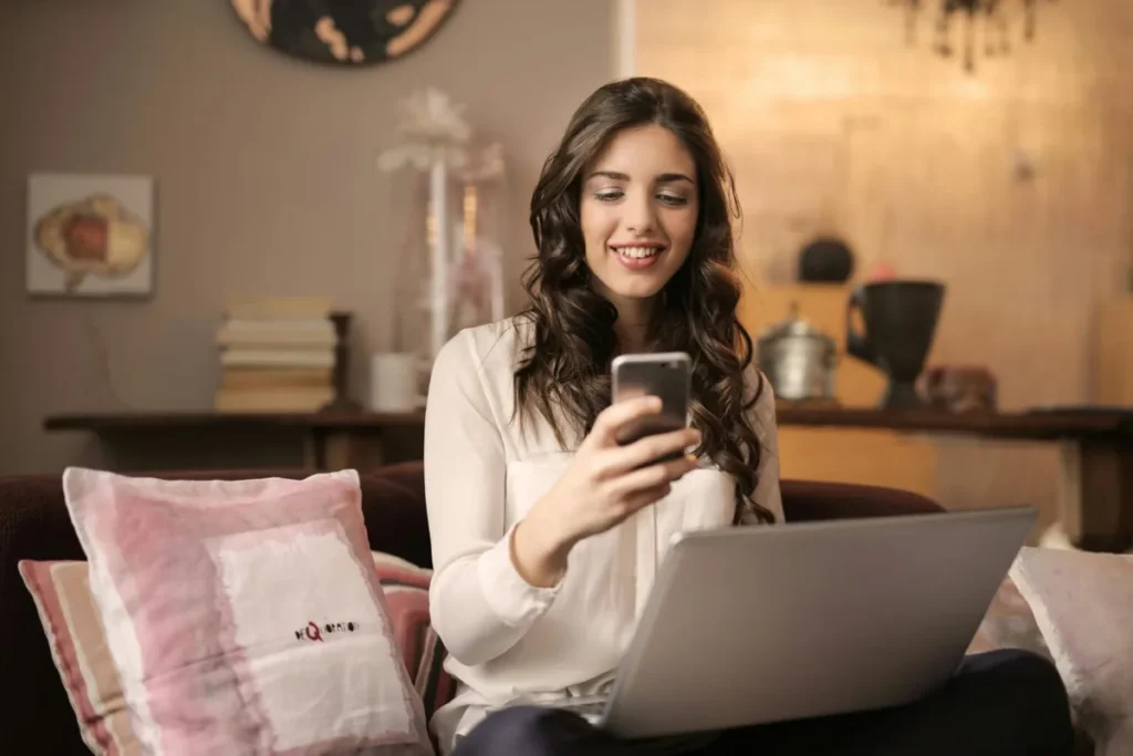 Woman sitting on a sofa checking her visa application on her phone and laptop