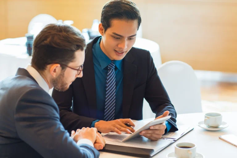 Foreign entrepreneur meeting with Thai business consultant and reviewing company setup options on a tablet.