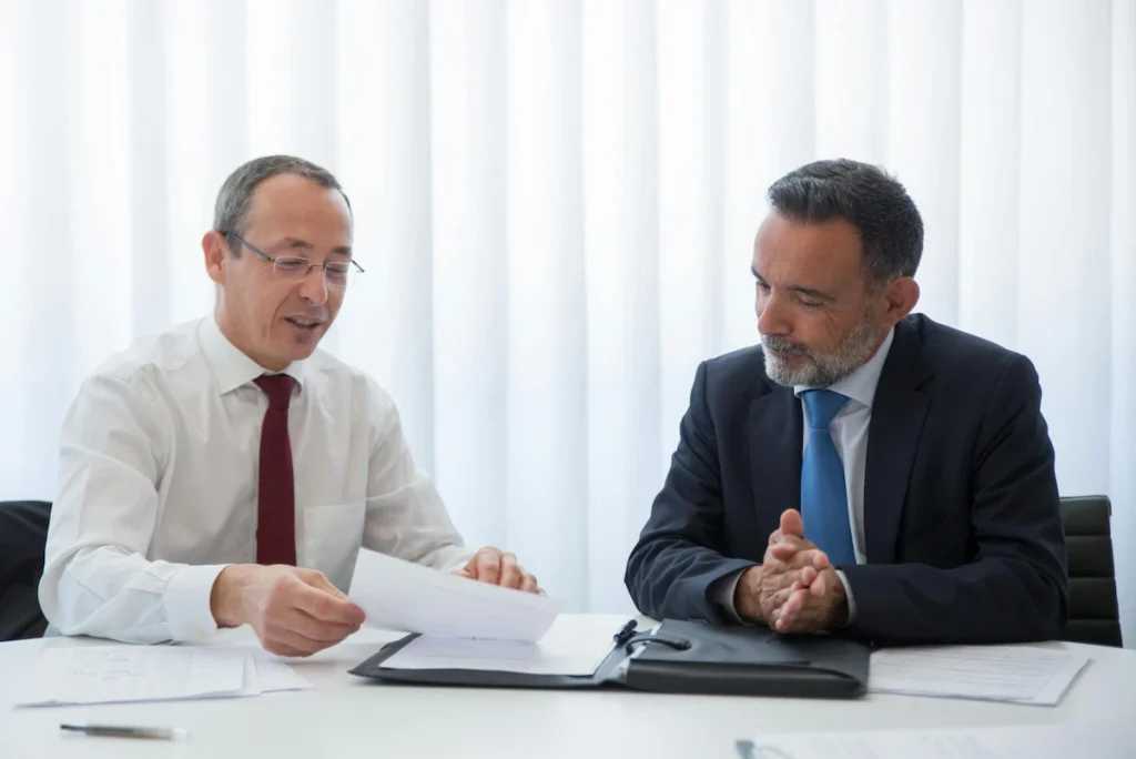 Two executives discussing documents during a formal meeting about starting a business in Thailand.