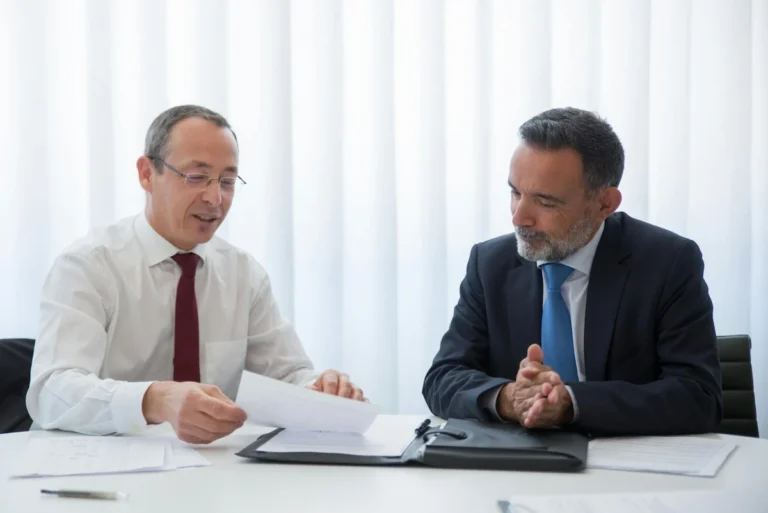 Two executives discussing documents during a formal meeting about starting a business in Thailand.
