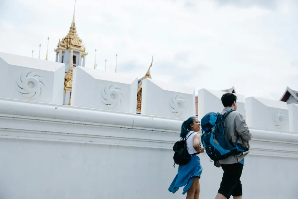 Travelers with backpacks walking past a Bangkok temple, documenting their journey and visa extension process in Thailand.