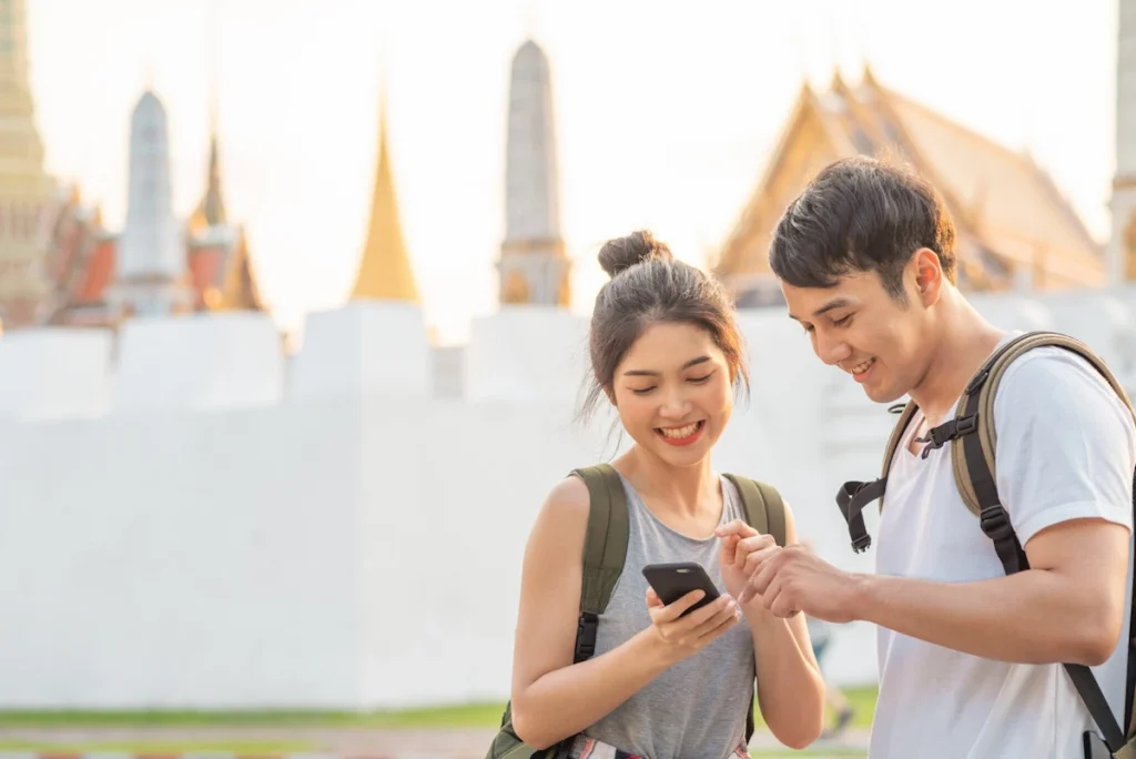 Young couple with backpacks checking visa or travel info on a smartphone in front of a Bangkok temple