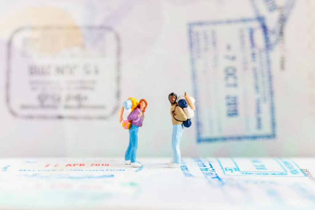 Miniature backpacker figures standing on passport visa stamps