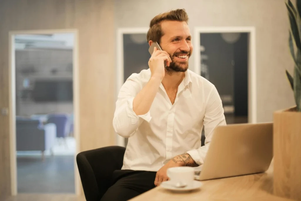 Smiling businessman talking on his phone while working on a laptop in a modern office